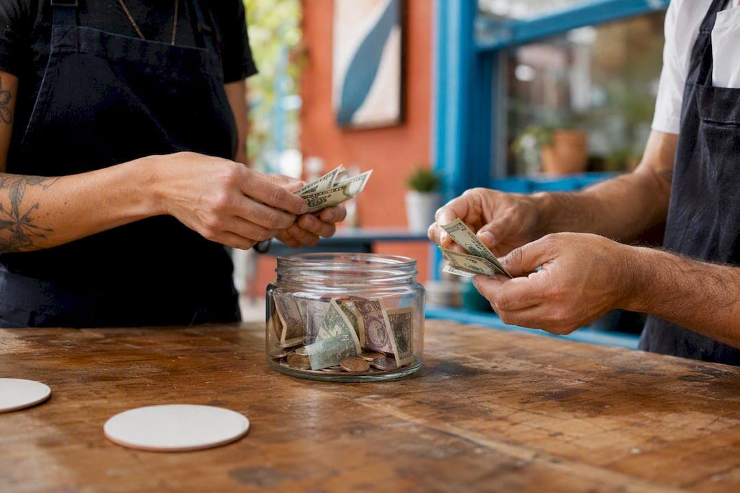 Hands distributing cash from tip pool jar